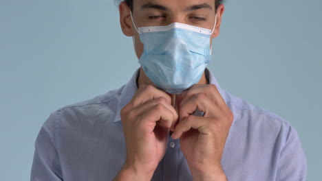 un hombre de aspecto profesional que usa su mascarilla quirúrgica parado correctamente sobre fondo azul - brote de coronavirus - toma de cierre