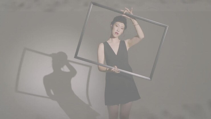 Donna che prende una struttura metallica, ruotandola e spostandola, proiettando un'ombra sotto una luce laterale per la moda.