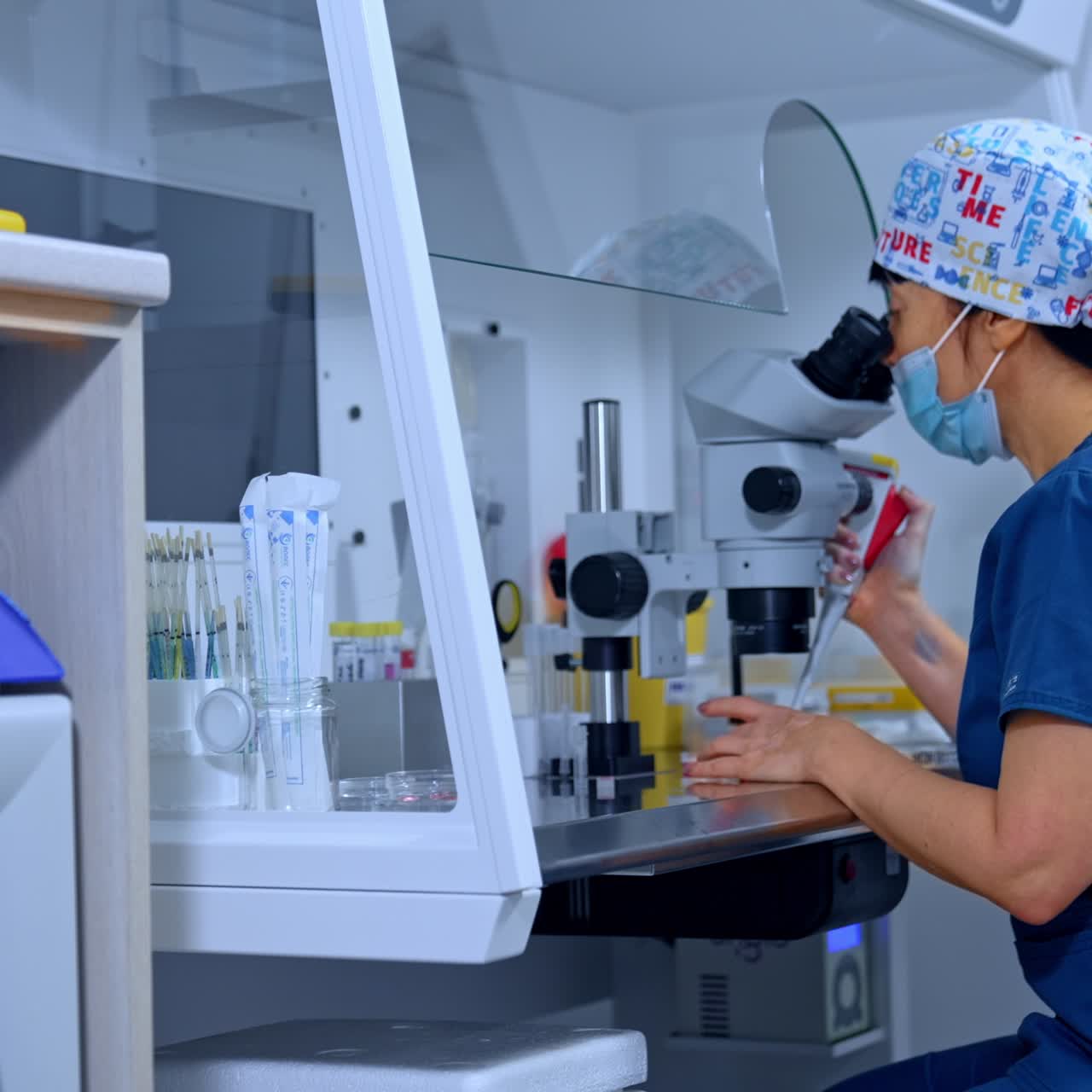 Female Caucasian doctor works using microscope. Medic looks at Petri dish applying a tool. Side view