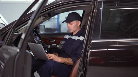 mecánico trabajando en una computadora portátil en un servicio de reparación de automóviles dentro del coche, de cerca