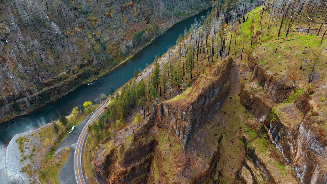 Flight above the beautiful rocks circled by the narrow river. Single car rides by the highway at the foot of the mountain. Top view.