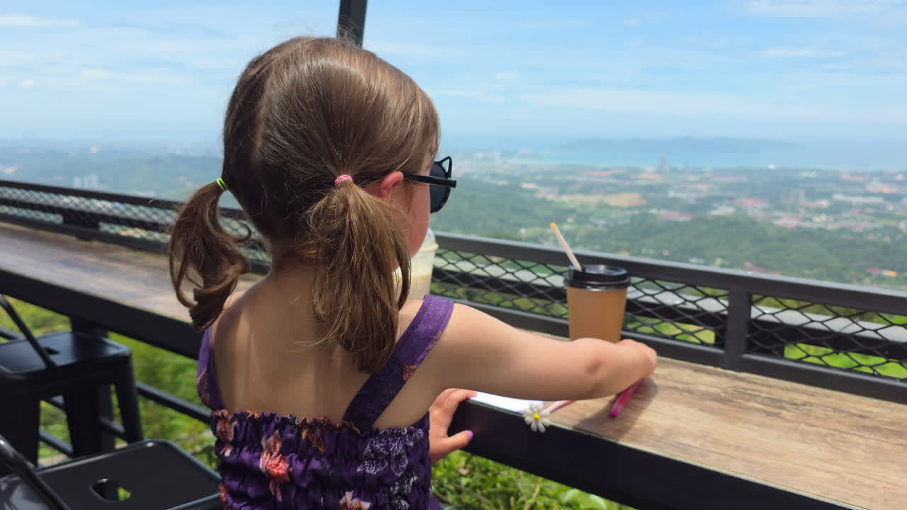 Adorable Young Girl Writing On Paper While On The Hillside Kokol Cafe In Kota Kinabalu, Sabah, Malaysia. Handheld Shot