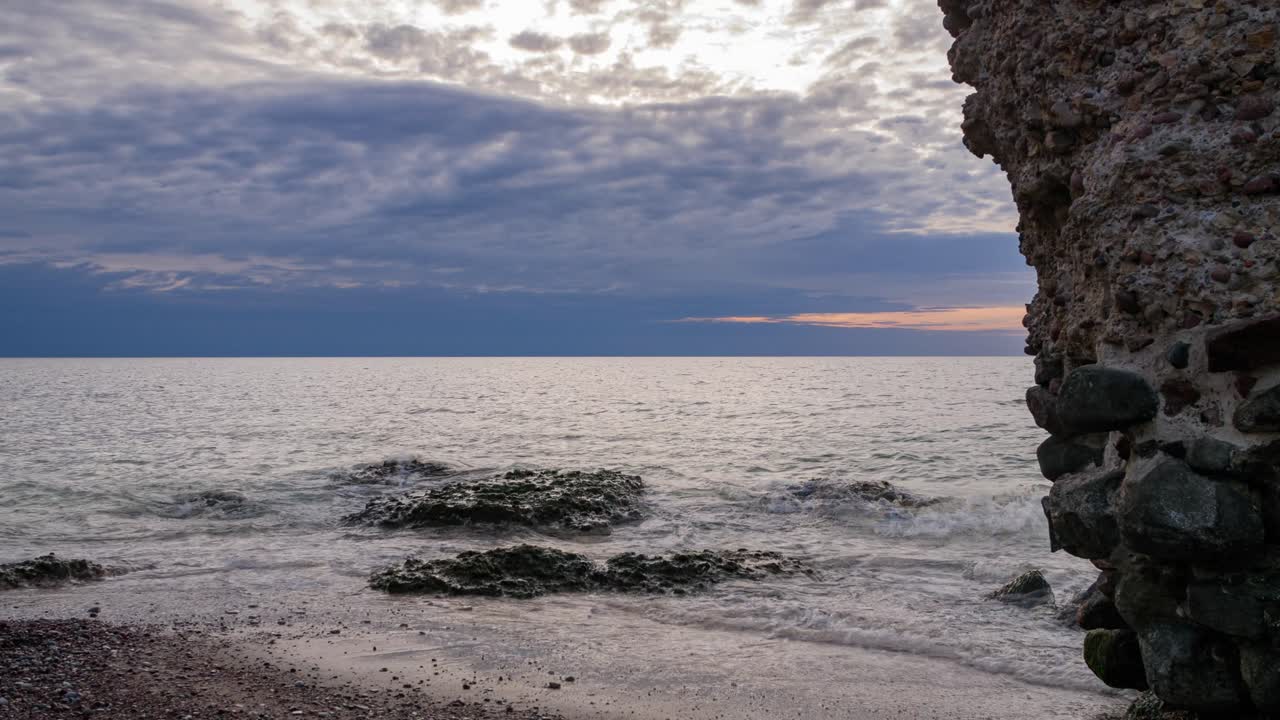 리파자(liepaja), 어두운 폭풍우 구름, 전경에 있는 오래된 요새 유적, 잔잔한 바다, 복사 공간, 낮은 각도 중간 와이드 샷에서 빠르게 움직이는 구름의 아름다운 활기찬 일몰 시간 경과