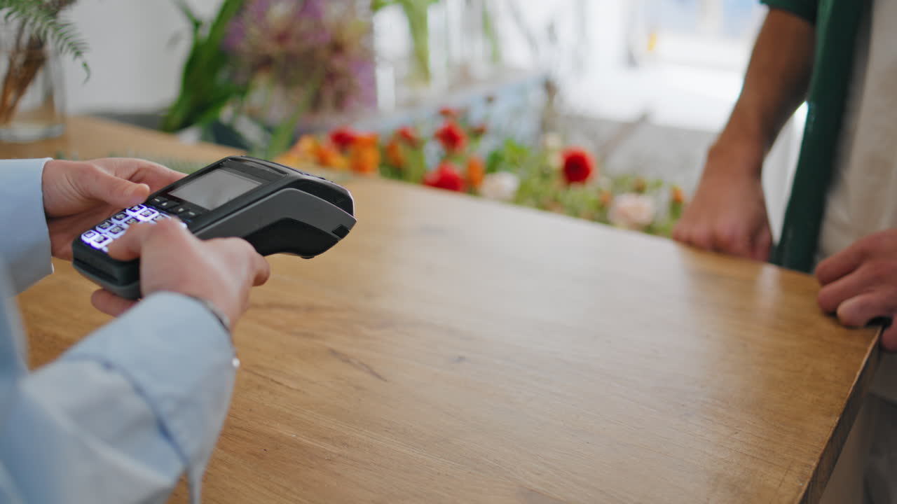 Closeup hands pay card contactless in flower shop. African customer spend money