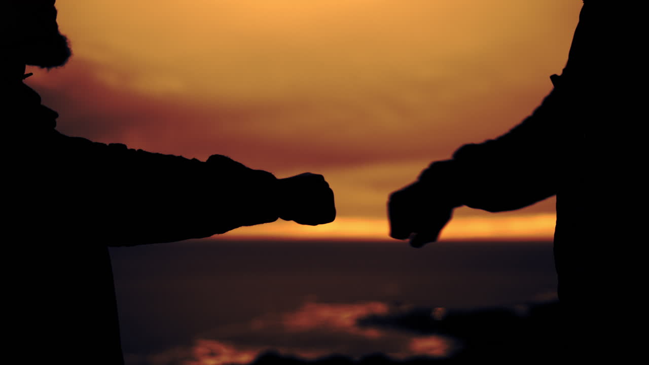People silhouetted against a sunset doing a fist bump