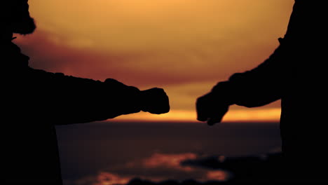 people silhouetted against a sunset doing a fist bump