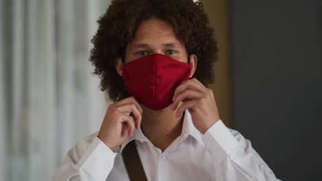 portrait of mixed race man with curly hair putting on red face mask