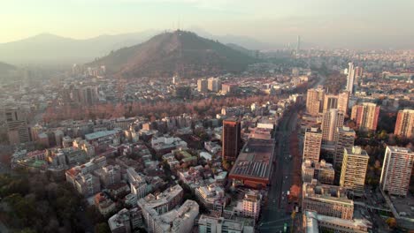 Aerial-dolly-in-of-Lastarria-neighbourhood-buildings,-traffic-in-Alameda-avenue-and-San-Cristobal-Hill-in-the-background,-Chile