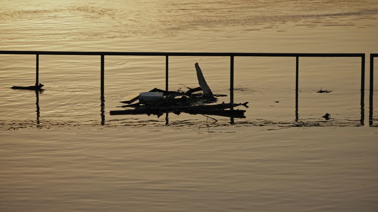 Debris floating against a submerged railing in floodwaters at sunset, Budapest, Hungary