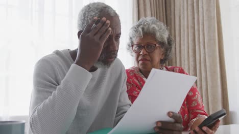 a senior african american couple at home working on papers in social distanci