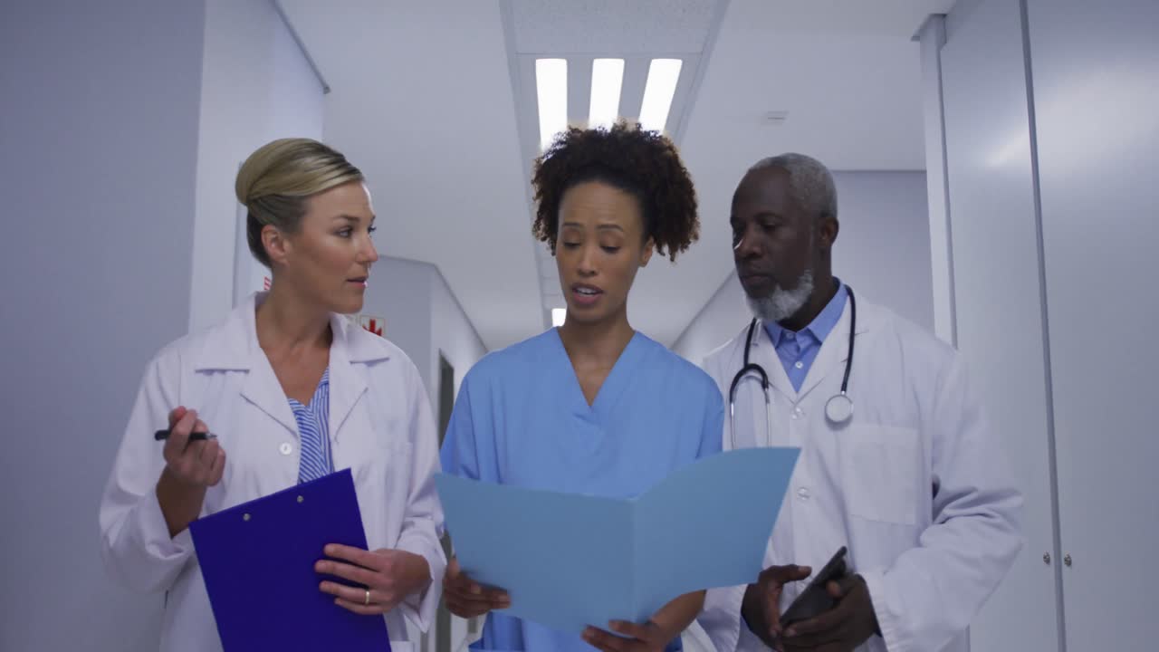 Diverse male and female doctors and medical staff walking hospital corridor looking at documents