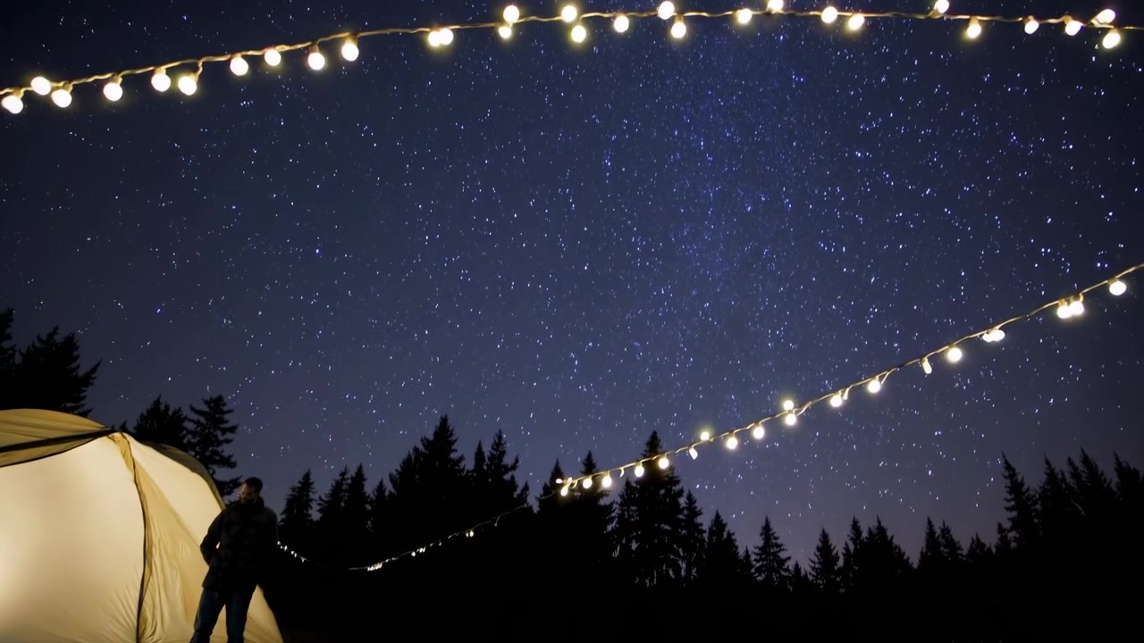 Person Standing Outside Illuminated Camping Tent Under Starry Night Sky