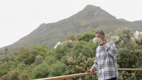 Senior-biracial-man-drinking-coffee-standing-on-balcony-with-mountain-view,-copy-space,-slow-motion