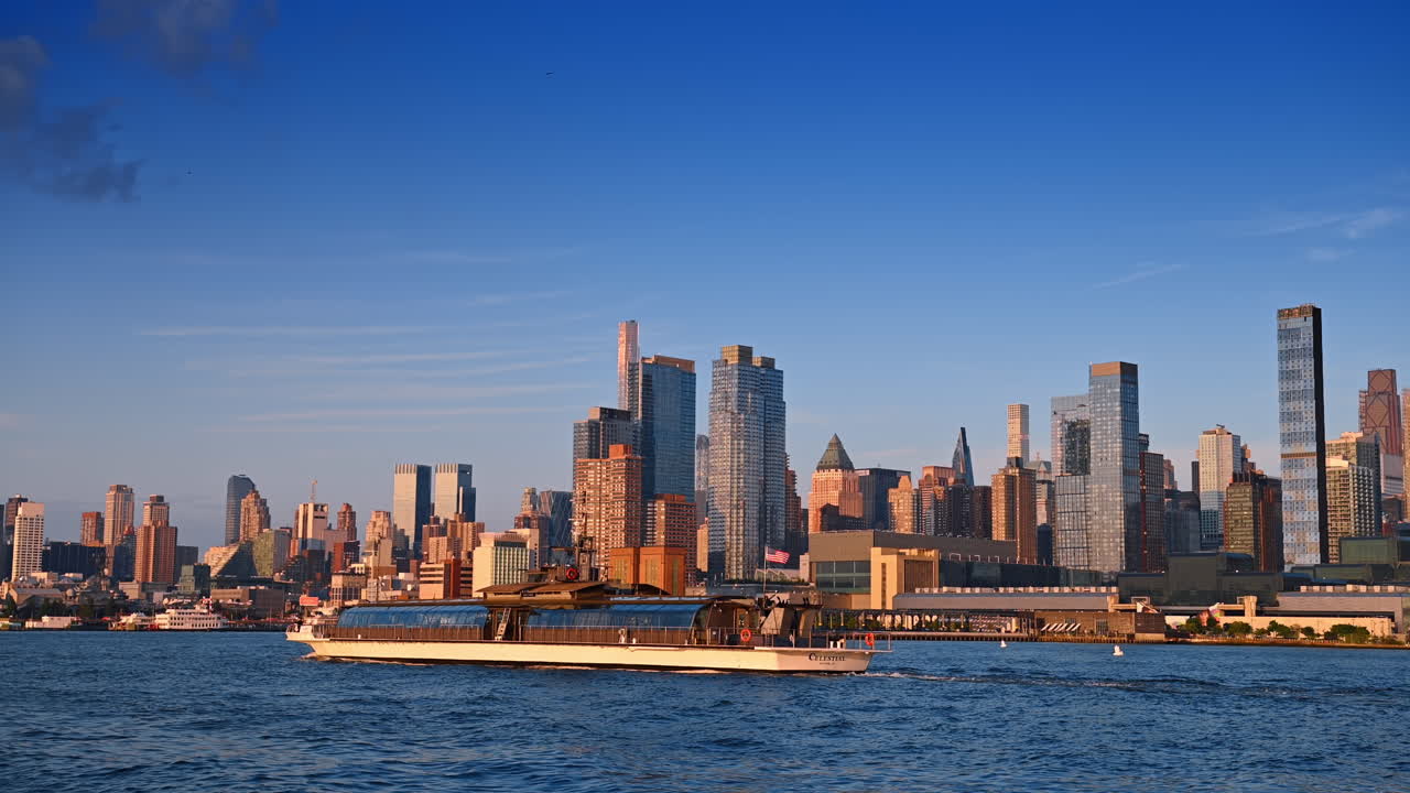 Lang flodbåd, der sejler langs flodlandskabet ved solnedgang. Tæt byhorisont i baggrunden, New York, USA