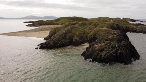 Vista-Aérea-De-órbita-Baja-Ynys-Llanddwyn-Island-Anglesey-Sendero-Costero-Con-Montañas-Snowdonia-A-Través-Del-Mar-Irlandés