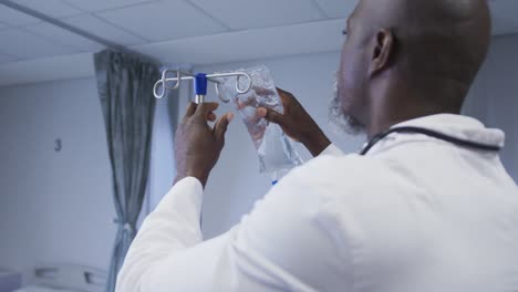 African-american-male-doctor-preparing-drip-bag-for-patient-in-hospital-room