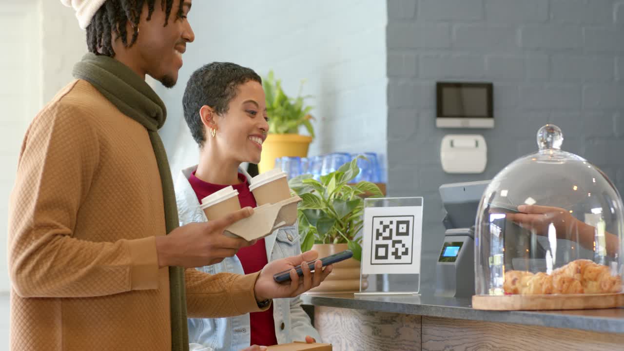 Scanning QR code Diverse couple tapping smartphone at coffee counter paying and grabbing pastry