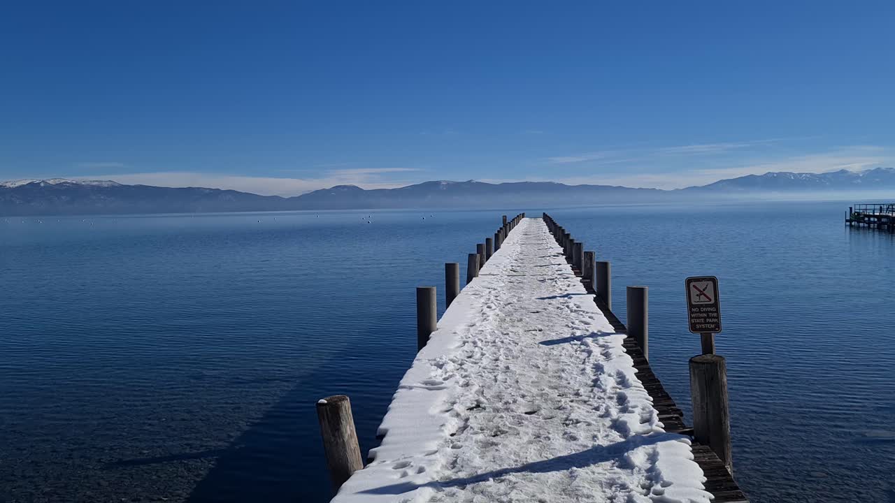 타호 호수 (lake tahoe) 연안의 은 겨울 날, 눈 인 도크, 조용한 파란 물, 그리고 지평선에 있는 산.