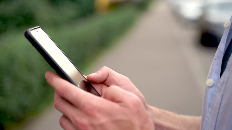 Primo piano di un uomo che usa il suo smartphone e sorride all'aperto.