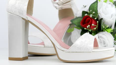 elegant luxury laced bridal wedding shoes and bouquet with red rose on white background closeup