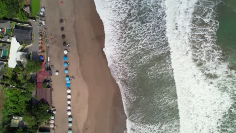 Batu-Belig-Beach-Coastline-with-Long-White-Foamy-Waves-Rolling-Over-Soft-Sand-In-Bali-Indonesia---aerial-top-down-flyover-along-shore