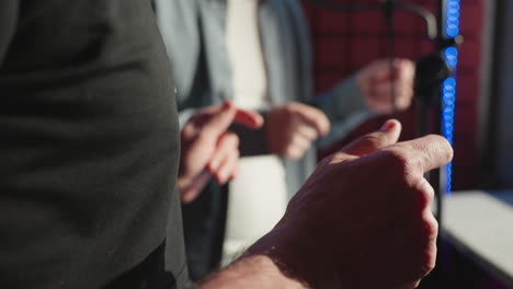 close-up of two men snapping their fingers rhythmically in a recording studio, focusing on their hands and casual attire. the background is slightly blurred