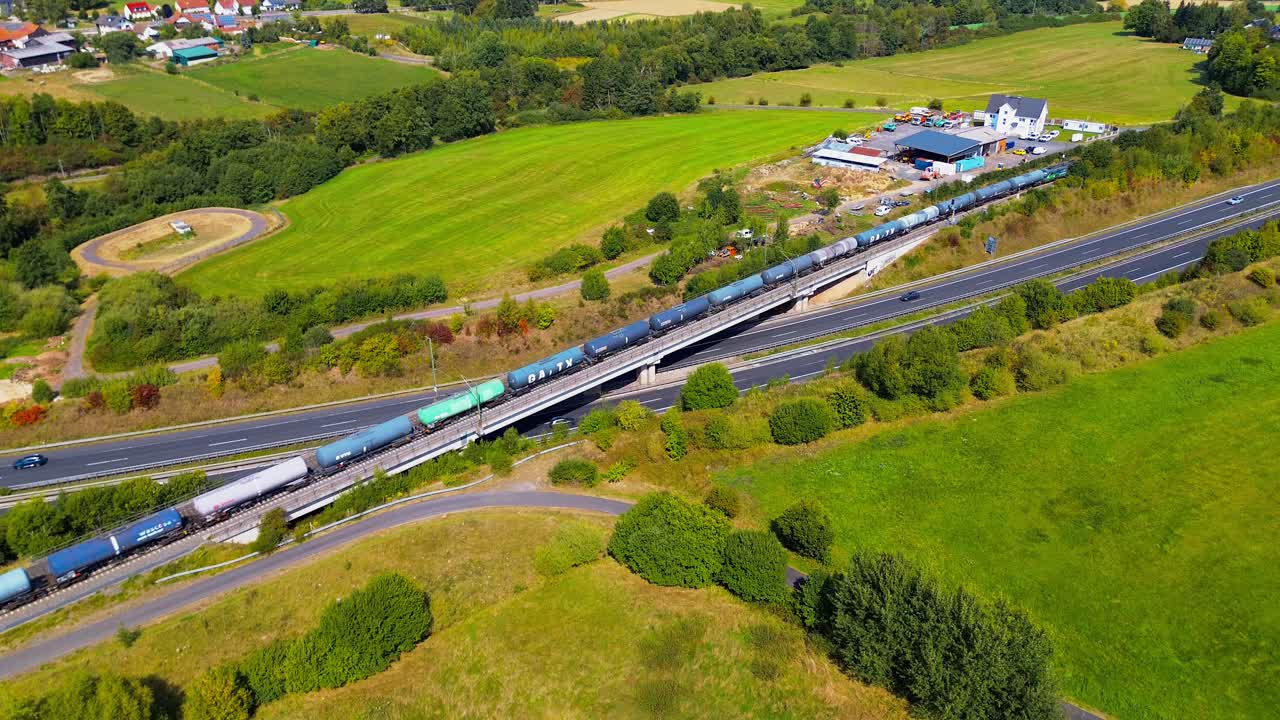 Aerial View of Freight Train with Tanker Cars Crossing Bridge Over Highway in Countryside