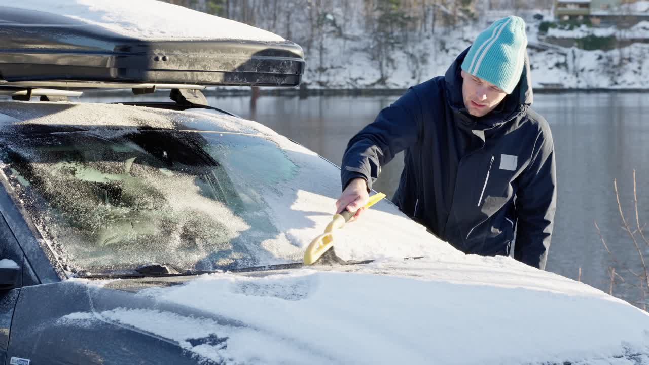 Norwegian man using brush and ice scraper to clear snow and ice from car windshield.