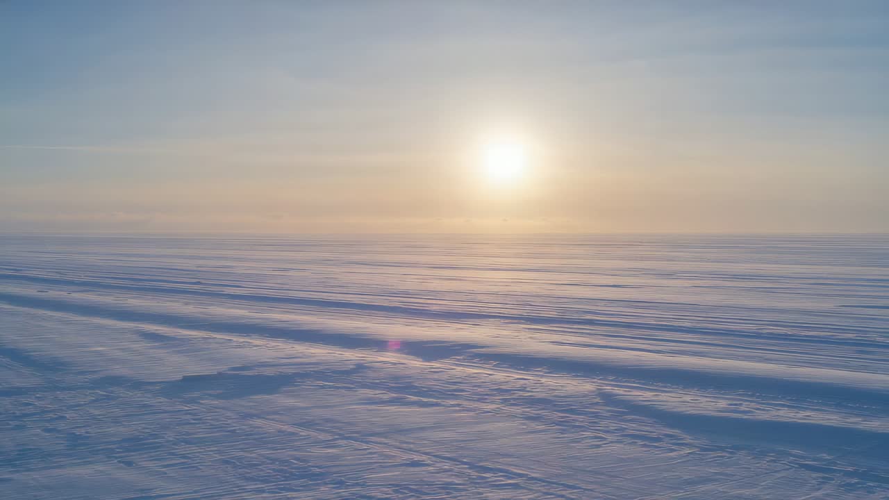 Panning camera moving slowly over frozen plain, showing low sun and parallel snow ridges at sunrise