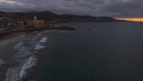 waves rolling on las canteras beach at sunset with alfredo kraus auditorium, las palmas, gran canaria