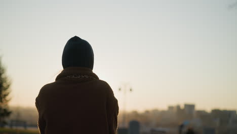 back shot of a woman walking faintly through a park at sunset, with the soft golden light of the setting sun casting a warm glow around her silhouette. the background is blurred