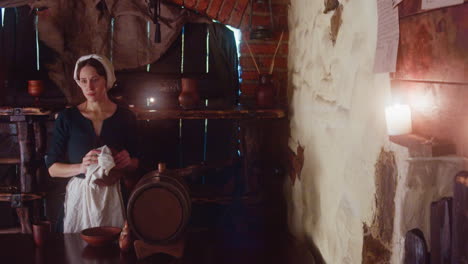 una camarera preocupada se limpia la frente en la taberna. una criada medieval en delantal limpia un cuenco de arcilla de pie en el mostrador de la casa de huéspedes. una mujer ocupada trabaja en una posada