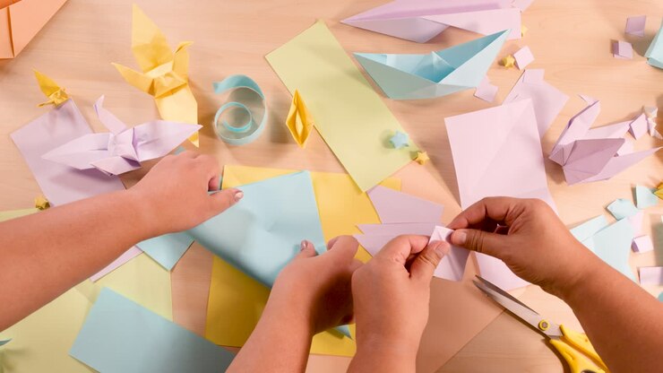Due persone piegano carta color pastello per origami su una scrivania, vista dall'alto, illuminazione soffusa