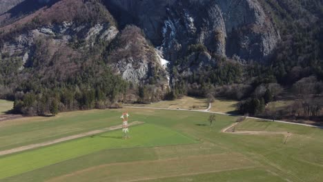 Aerial-approach-of-power-lines-and-red-and-white-electric-tower,-next-to-Arpenaz-waterfall,-Sallanches,-Haute-Savoie,-French-Alps