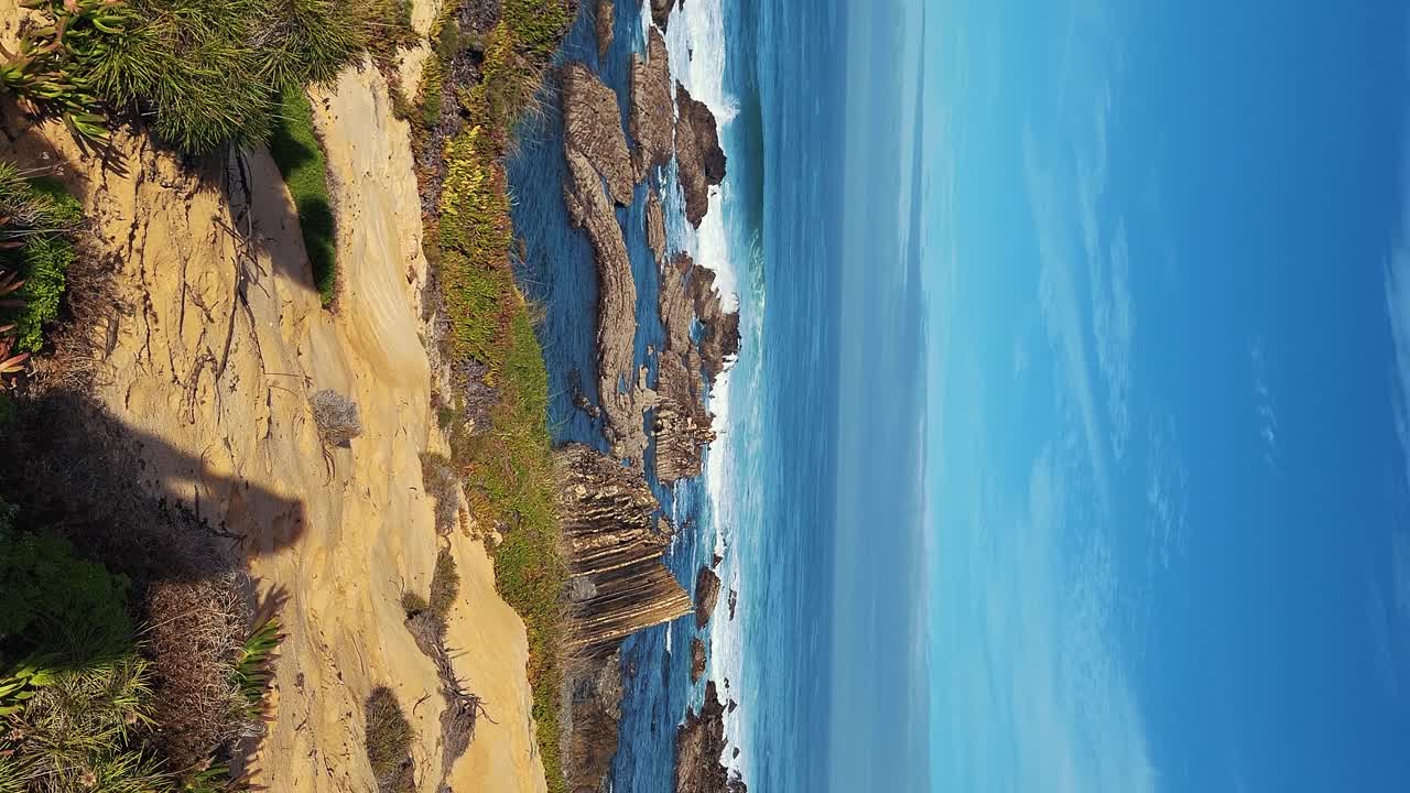 zambujeira do mar sobre la orilla del mar con olas del océano, acantilados y dunas de arena cubiertas de vegetación verde hojas rojas de higo agrio, día soleado, cielo azul claro