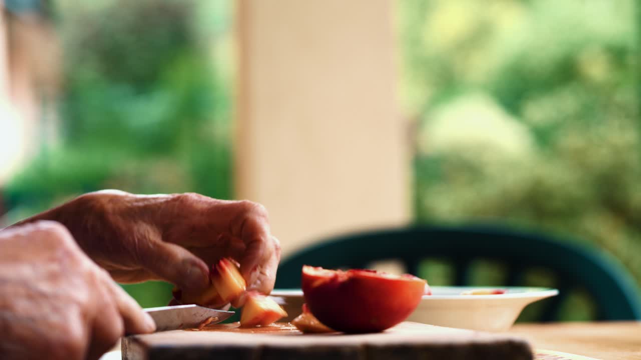 Close up of wrinkled hands of an old grandmother woman preparing a peach fruit on a cutting board