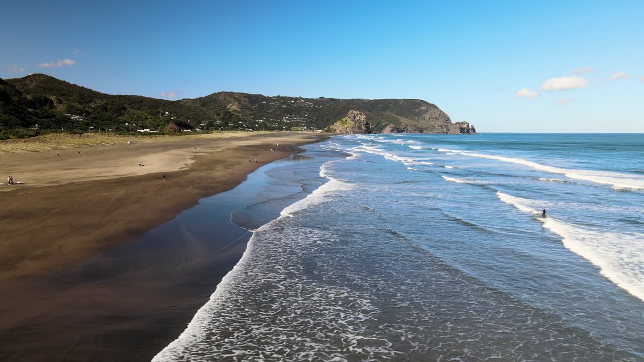 panorámica a través de la playa de arena negra de piha con el reflejo de un surfista saliendo del agua del océano