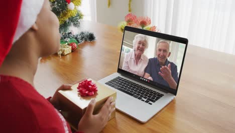 Afroamerikanische-Frau-Mit-Weihnachtsmütze-Nutzt-Laptop-Für-Weihnachtsvideoanruf-Mit-Paar-Auf-Dem-Bildschirm