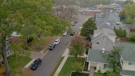 aerial of a car driving away down the street in a suburban neighborhood on an autumn day