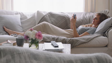 Hermosa-Mujer-Usando-Un-Teléfono-Inteligente-Relajándose-En-Un-Sofá-En-Casa-Navegando-En-Línea-Enviando-Mensajes-De-Texto-En-Las-Redes-Sociales-Disfrutando-De-La-Comunicación-Por-Teléfono-Móvil-Acostada-En-El-Sofá-Imágenes-De-4k