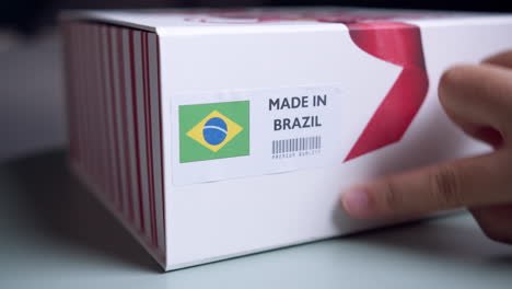 manos aplicando la etiqueta de la bandera hecha en brasil en una caja de cartón de envío con productos