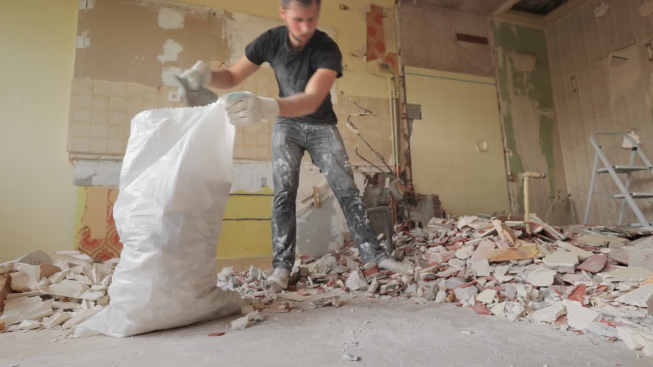 Male worker cleaning up renovation site indoor with a shovel inside a rubble bag