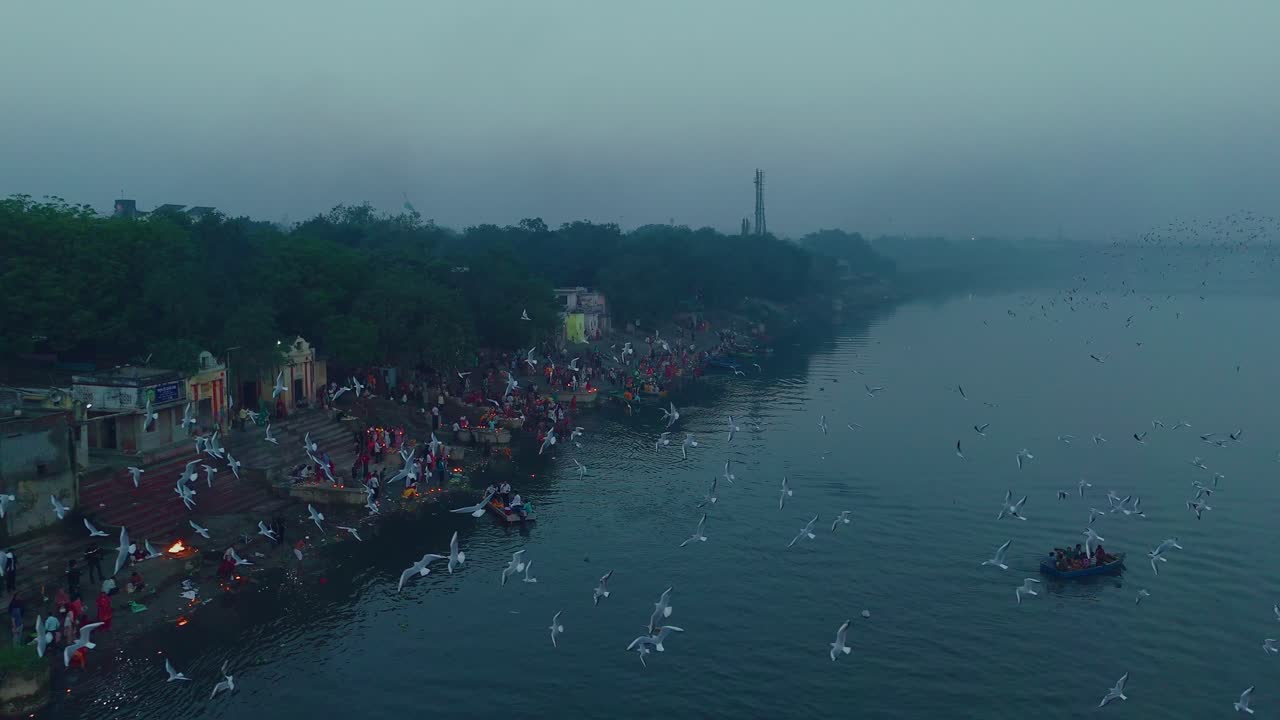 Letecký pohled na ghát Yamuna za zimního rána, představující tradiční lodě, chrám a ranní rituál