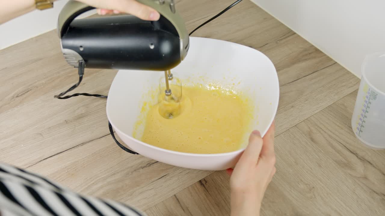 Whisking egg yolks in white bowl with hand mixer for dessert preparation at home