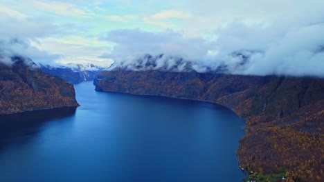 cloud-covered mountain peaks and calm blue fjord during autumn season in norway