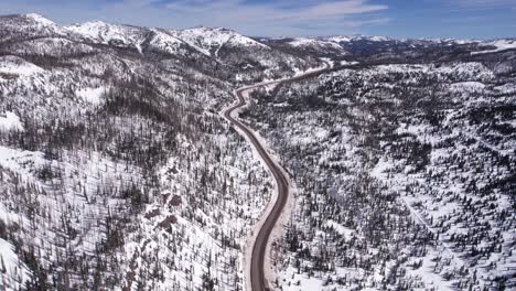 drone shot on mountain road pass on sunny winter day snow capped hills and pines