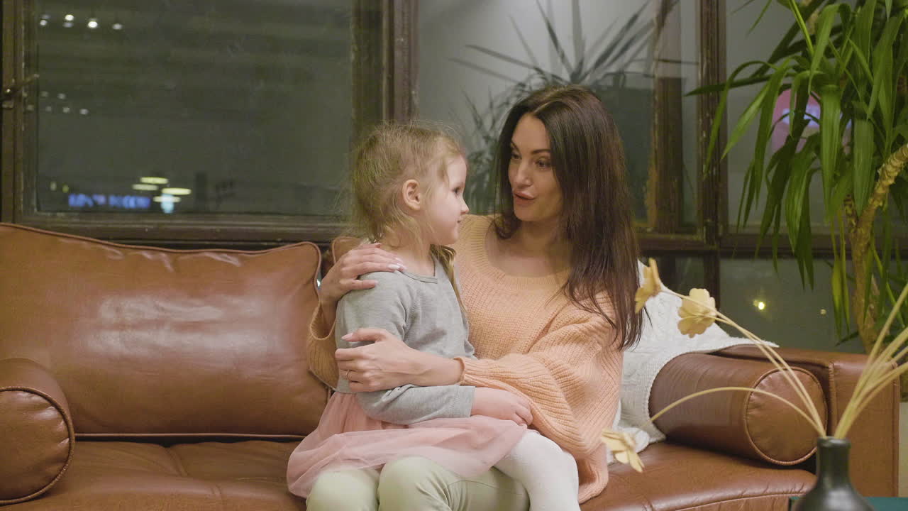Mamma felice seduta sul divano con la sua bambina che parla con lei.