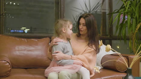 happy mother sitting on sofa with her little daughter and talking with her