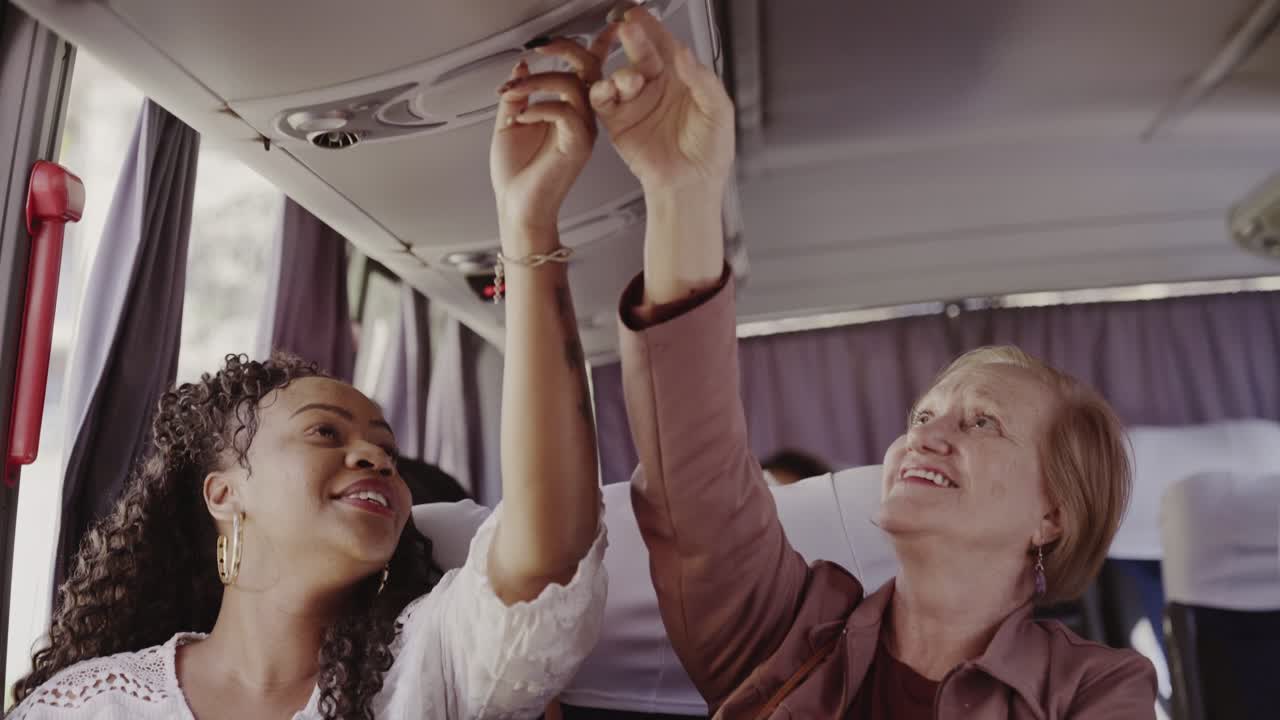 Two Women Adjusting Overhead Controls on a Bus