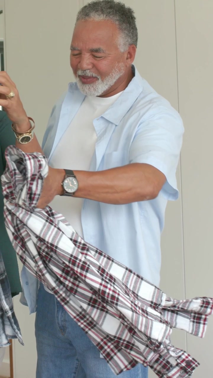 Video verticale: Uomo in camicia blu che tiene in mano una camicia a quadri e la offre alla partner in camera da letto, vestiti.